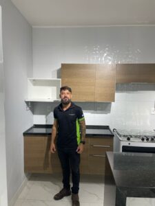 Trabalhador uniformizado da FR Montagens posa ao lado dos armários da cozinha montados em perfeito estado